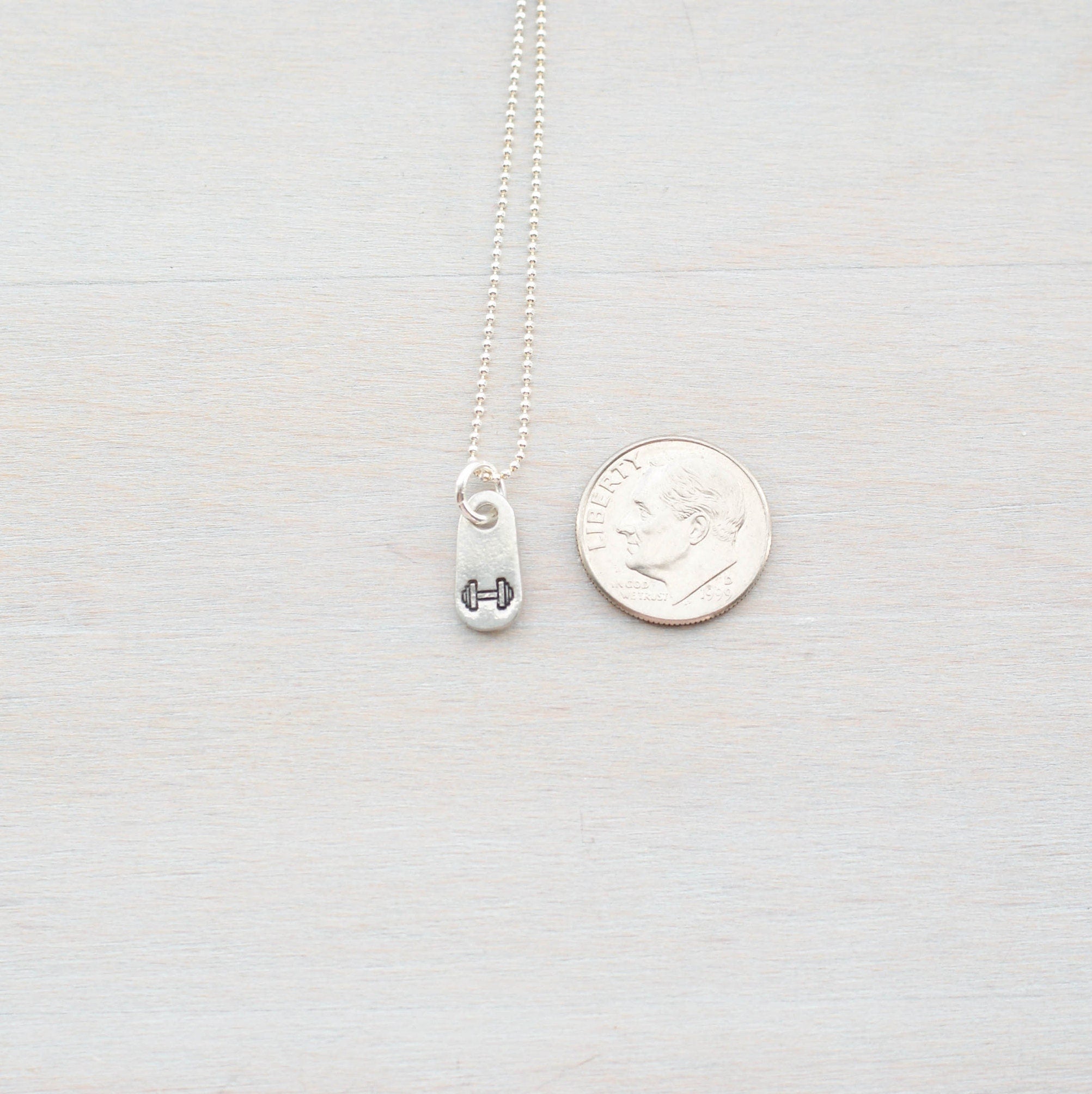 Silver fitness jewelry dumbbell necklace in artisan pewter next to dime