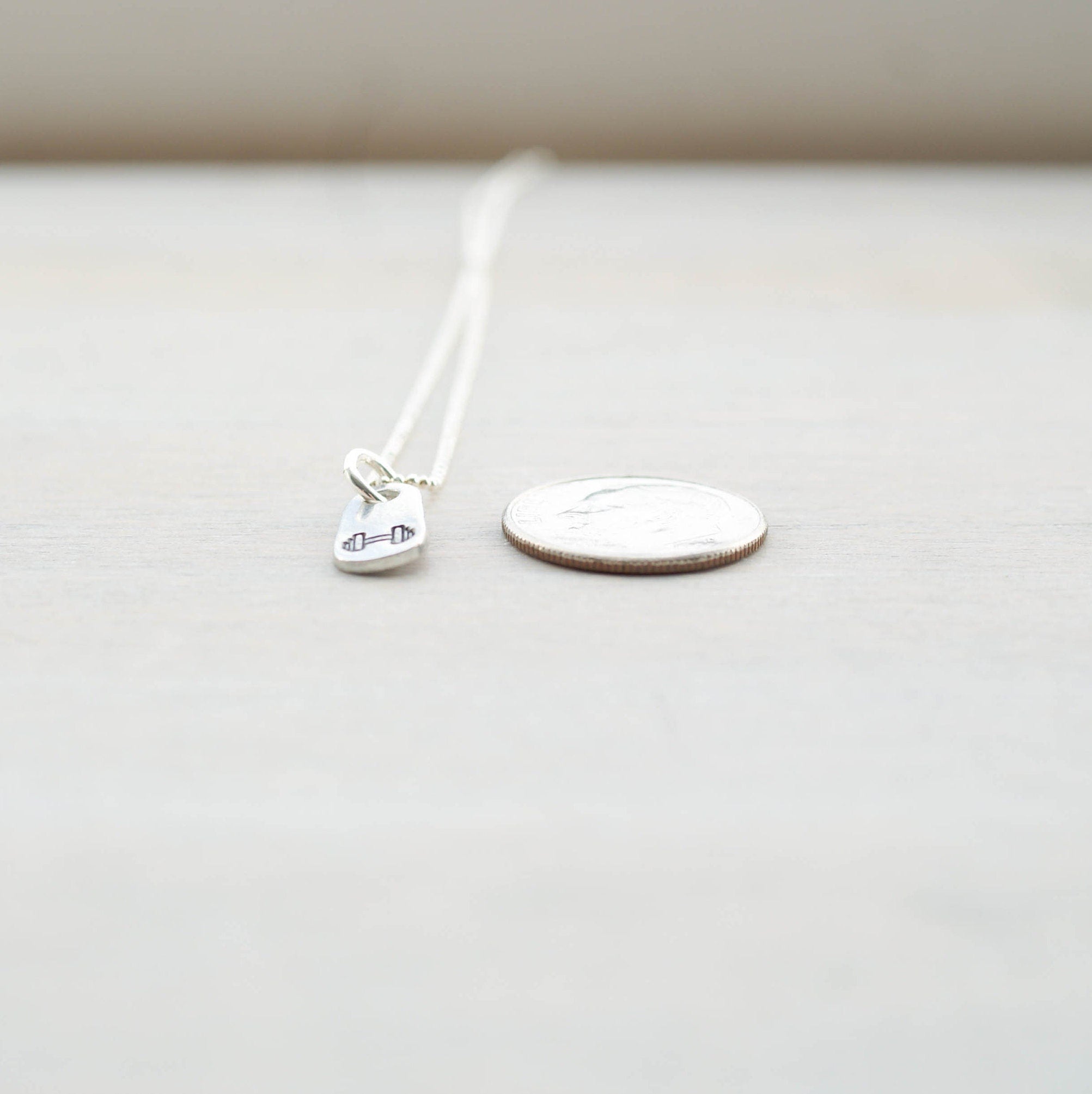 Silver dumbbell fitness necklace in artisan pewter next to dime