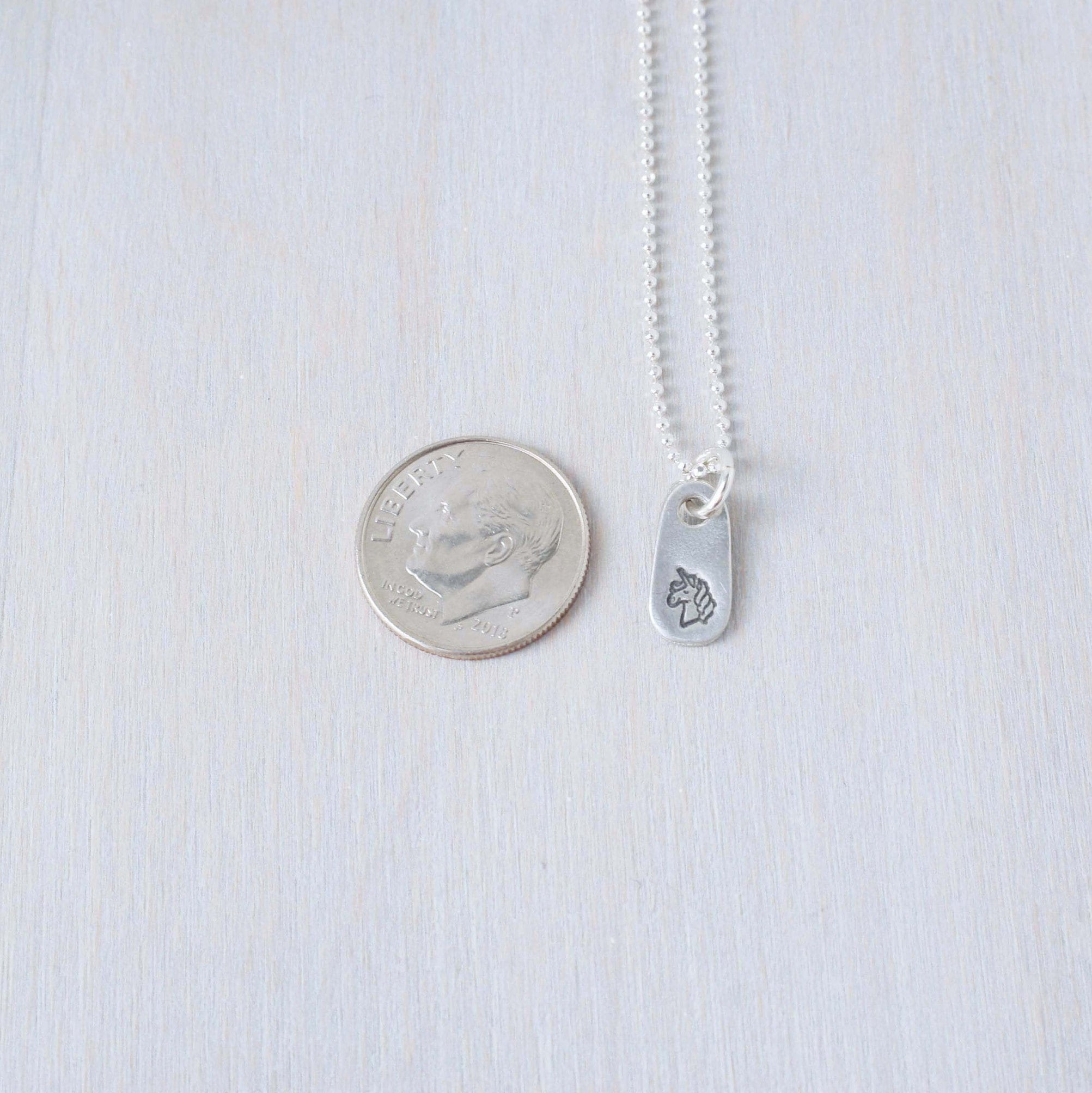 Silver unicorn necklace in artisan pewter next to dime