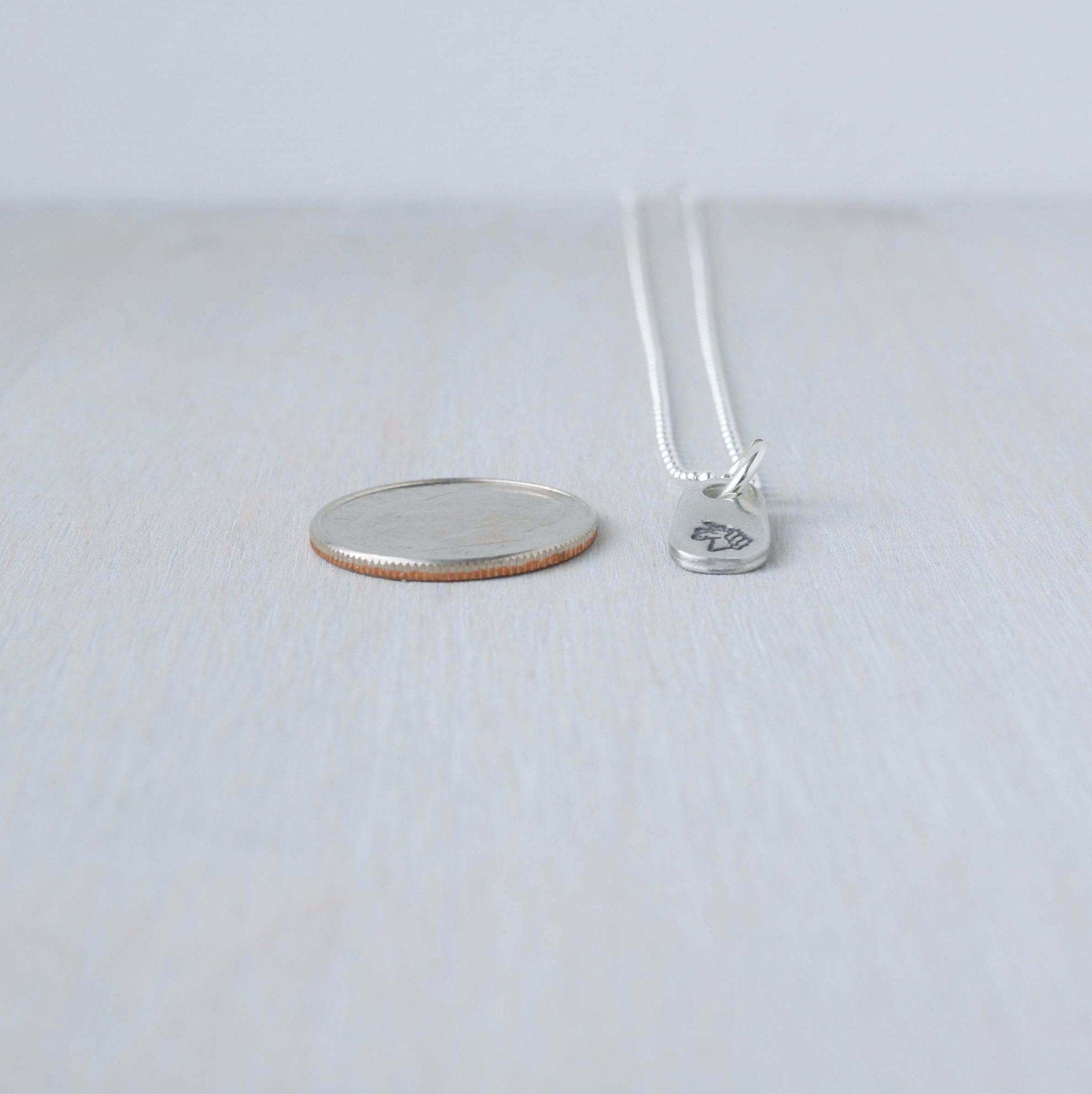 Silver unicorn necklace in artisan pewter next to dime