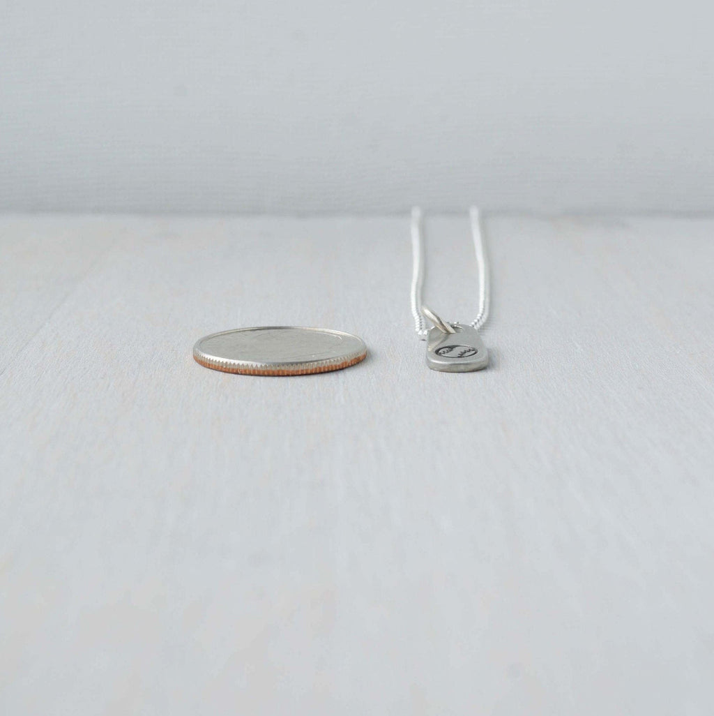 Silver baseball necklace in artisan pewter next to dime