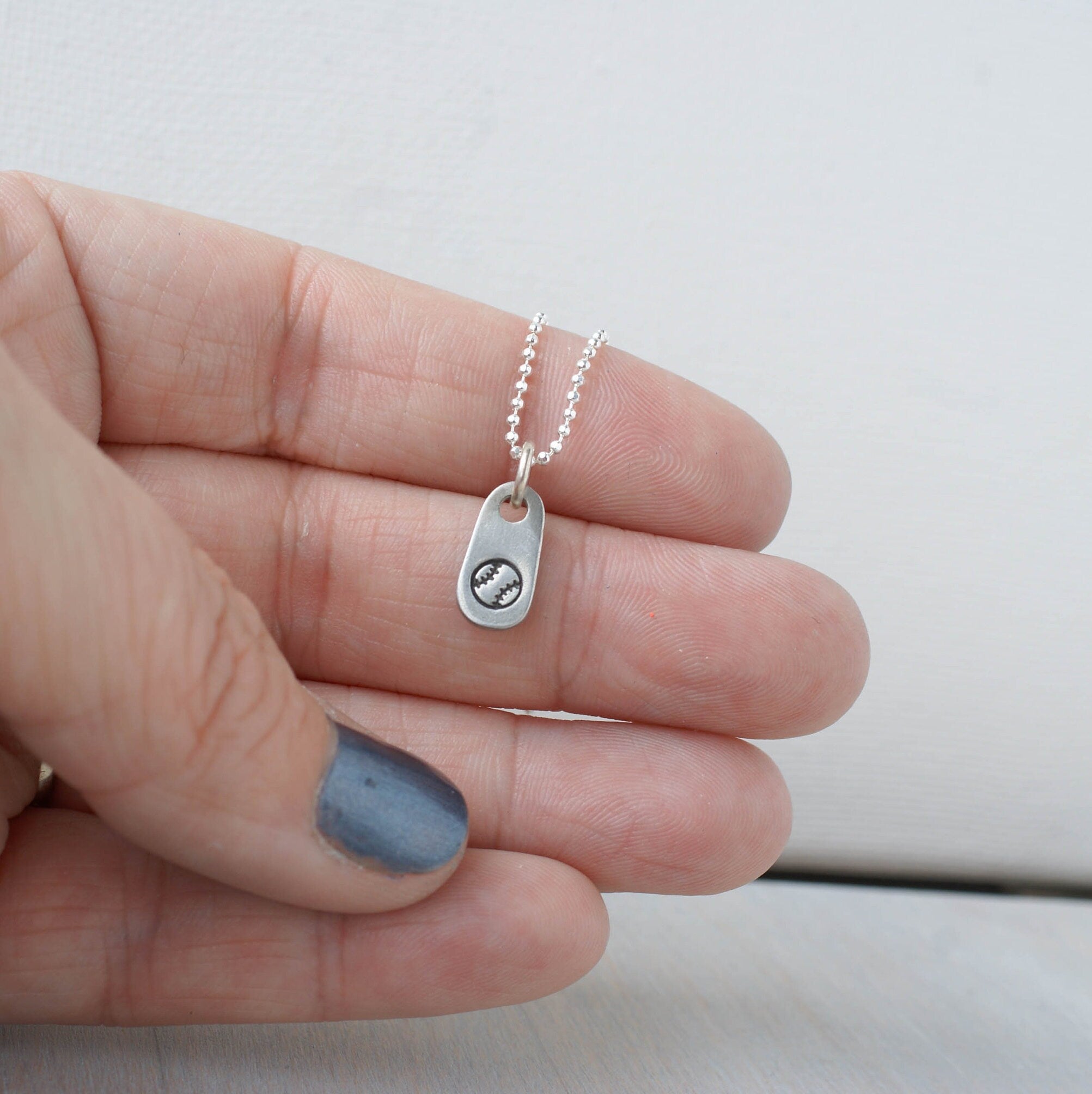 Silver softball necklace in artisan pewter in hand