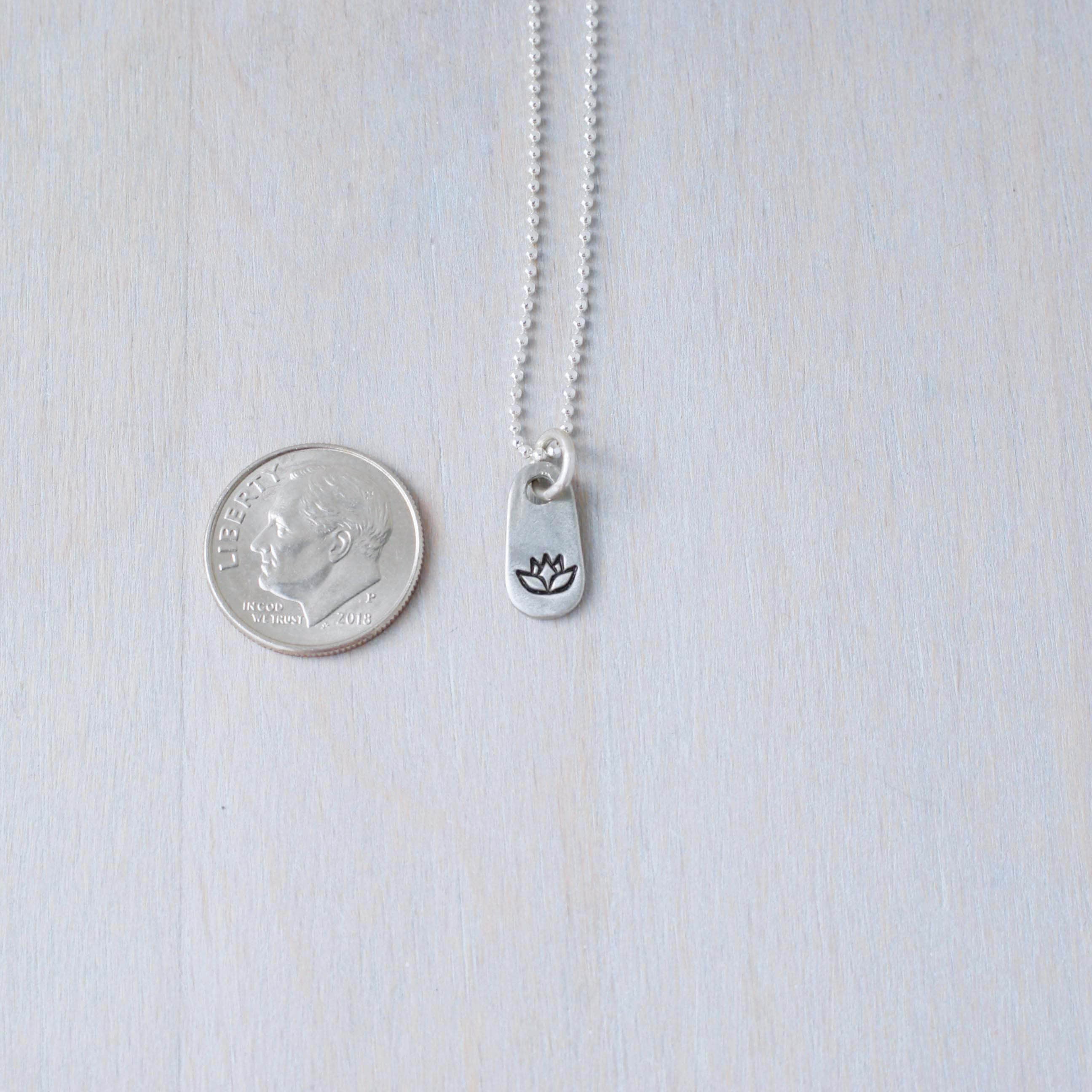 Silver lotus necklace in artisan pewter next to dime