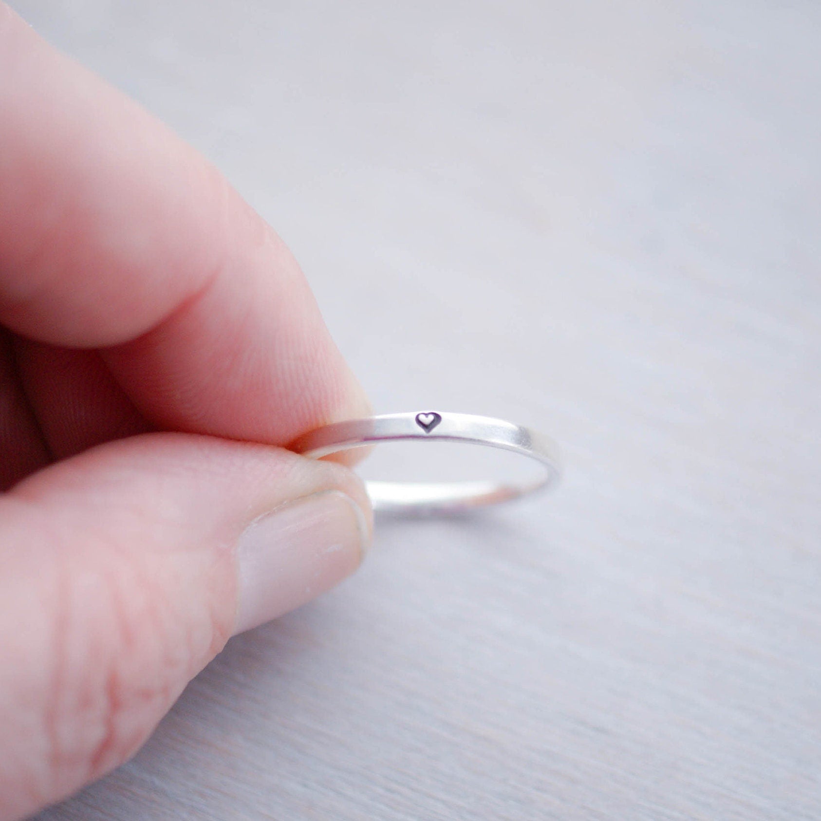 Sterling silver ring stamped with small heart held between fingers