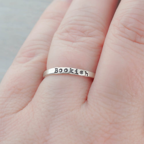 Silver ring with 'Bookish' engraving on a person's finger against a neutral background