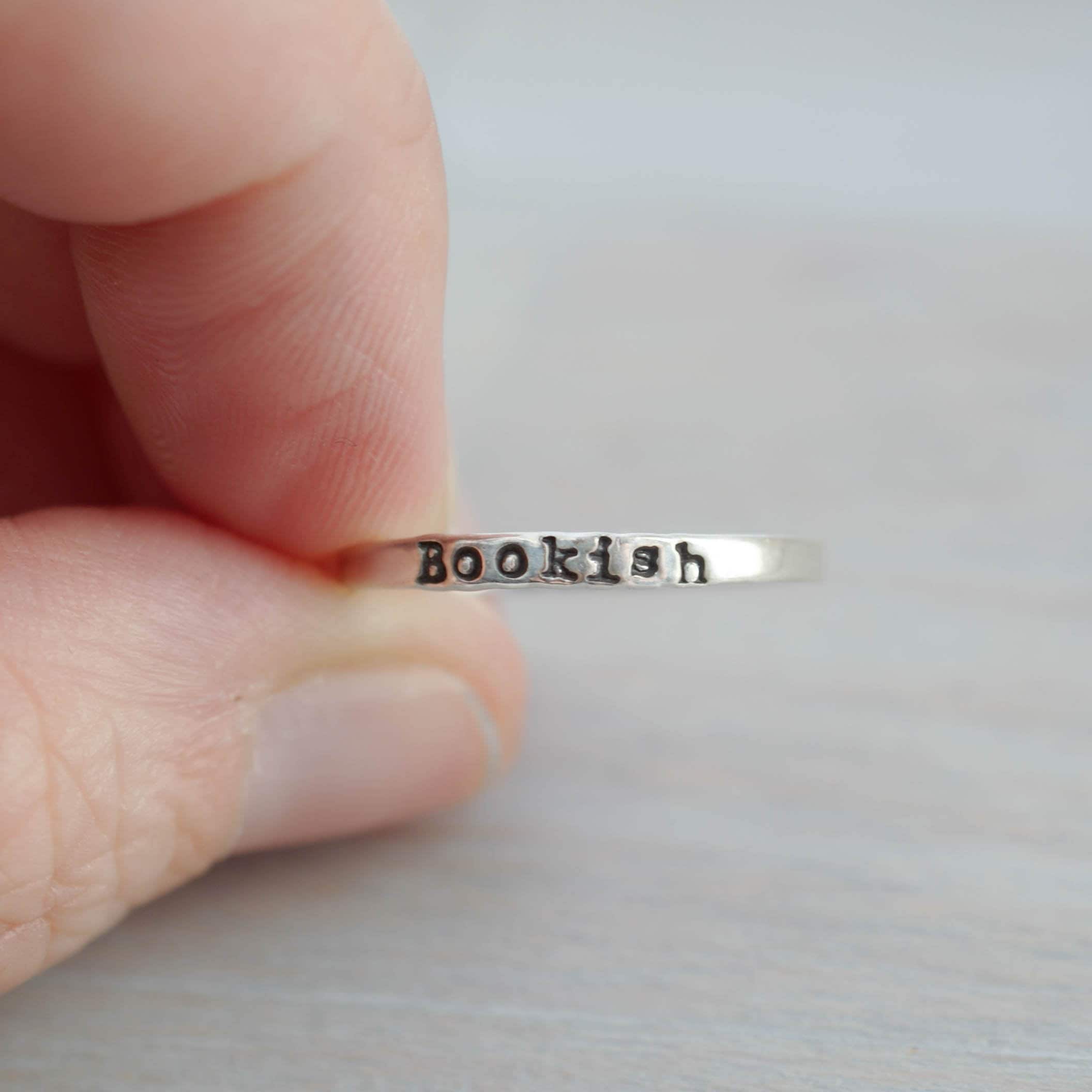 Silver ring with 'bookish' engraving held between fingers on a light background