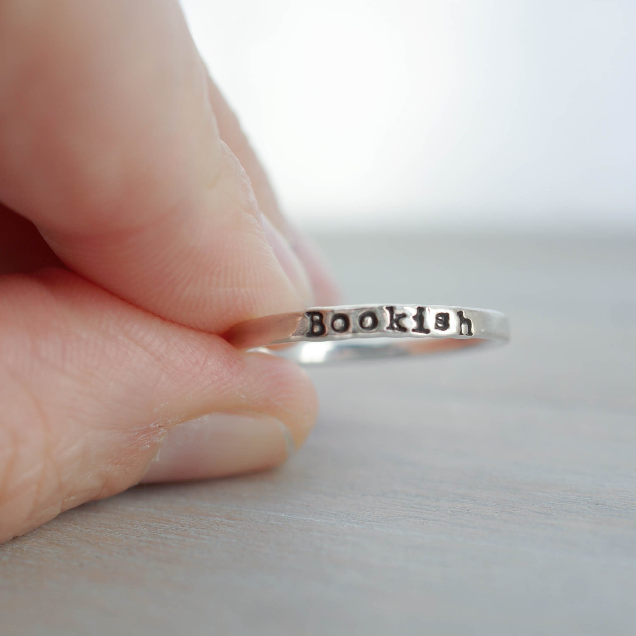 Silver ring with 'Bookish' engraving on a finger against a neutral background
