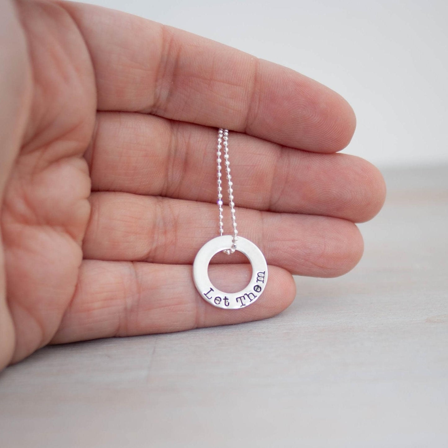 Image of Let Them Words of Affirmation Sterling Silver Necklace being held in hand.