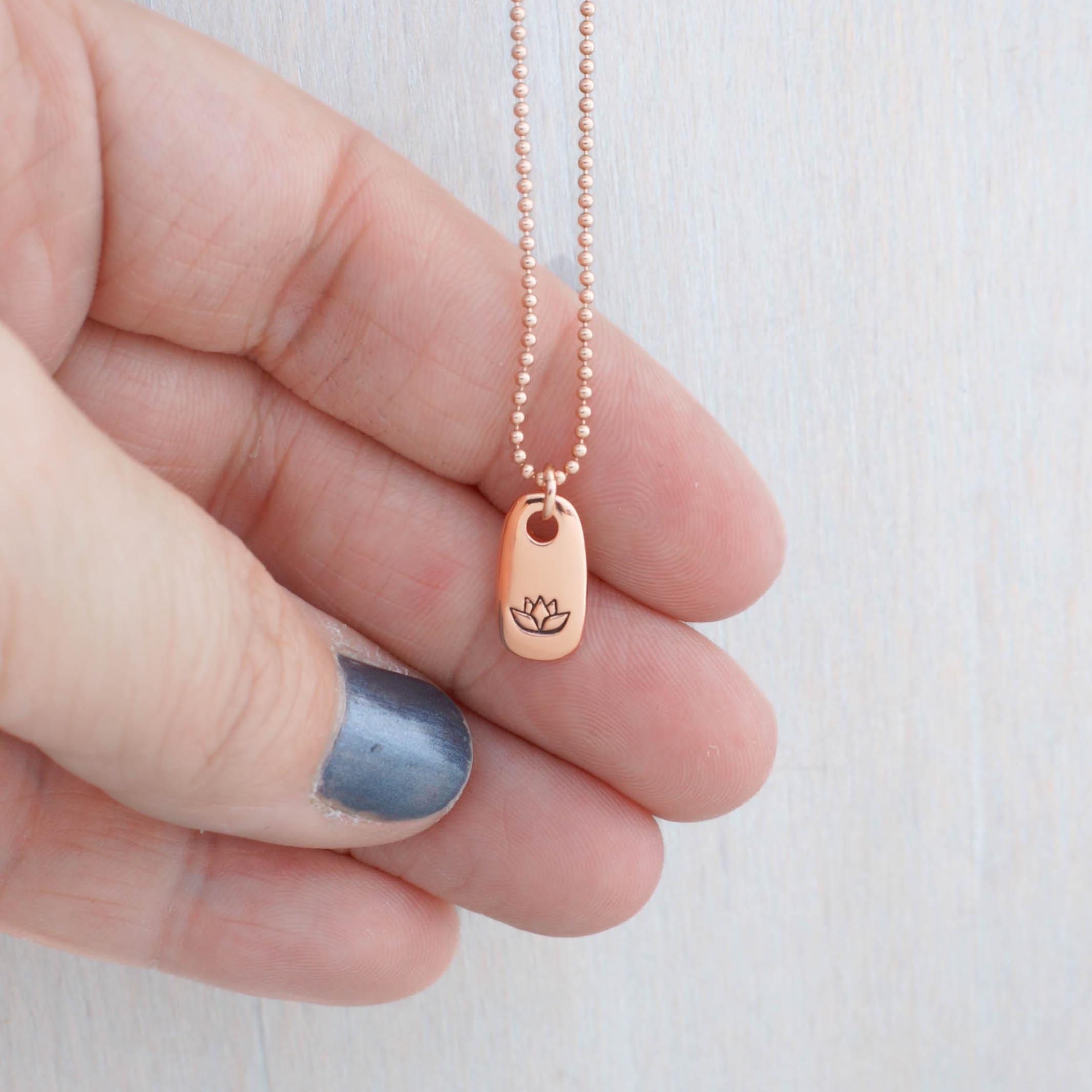 Image of Rose gold small tag necklace stamped with lotus flower being held in hand