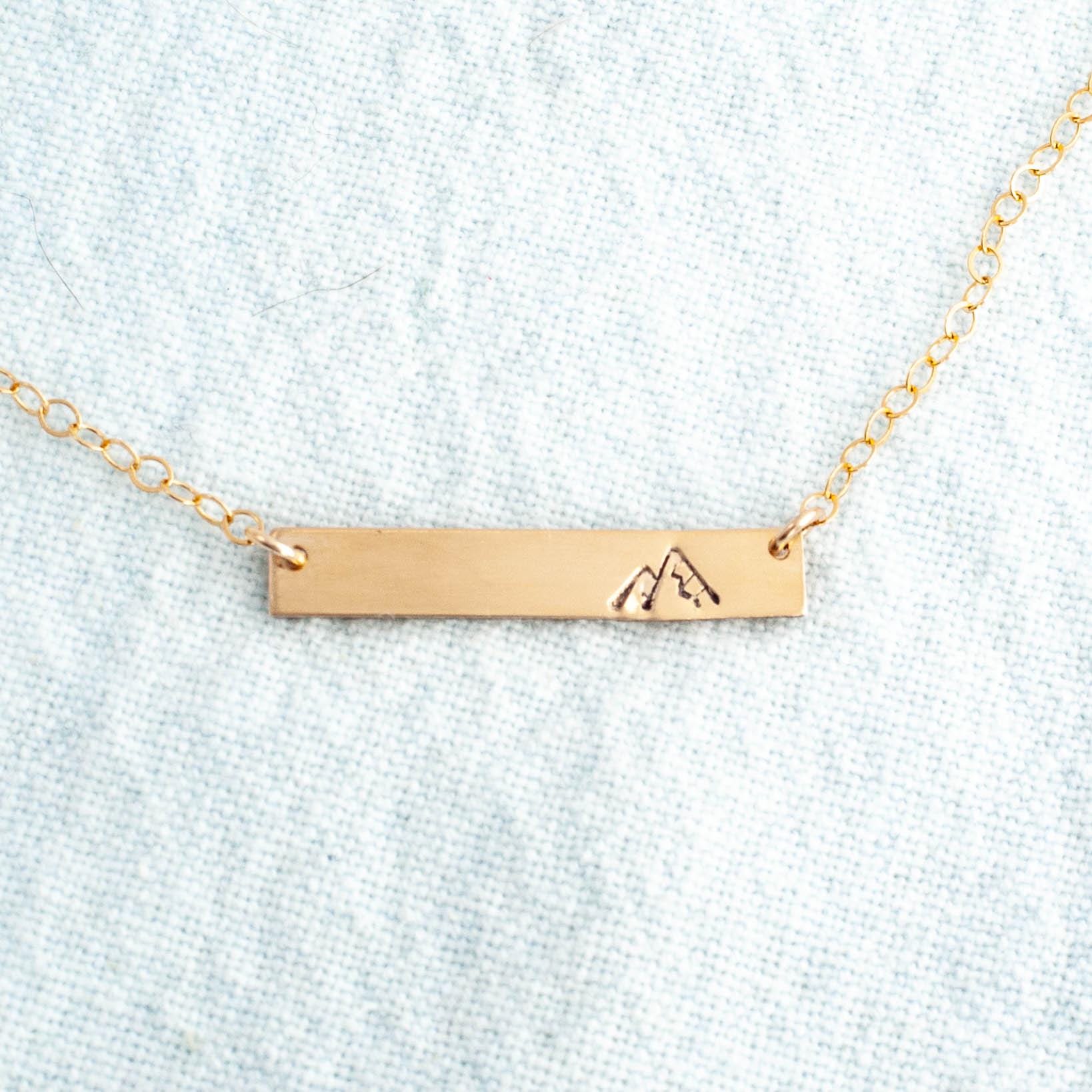 Image of gold necklace with mountain stamped on the right side.