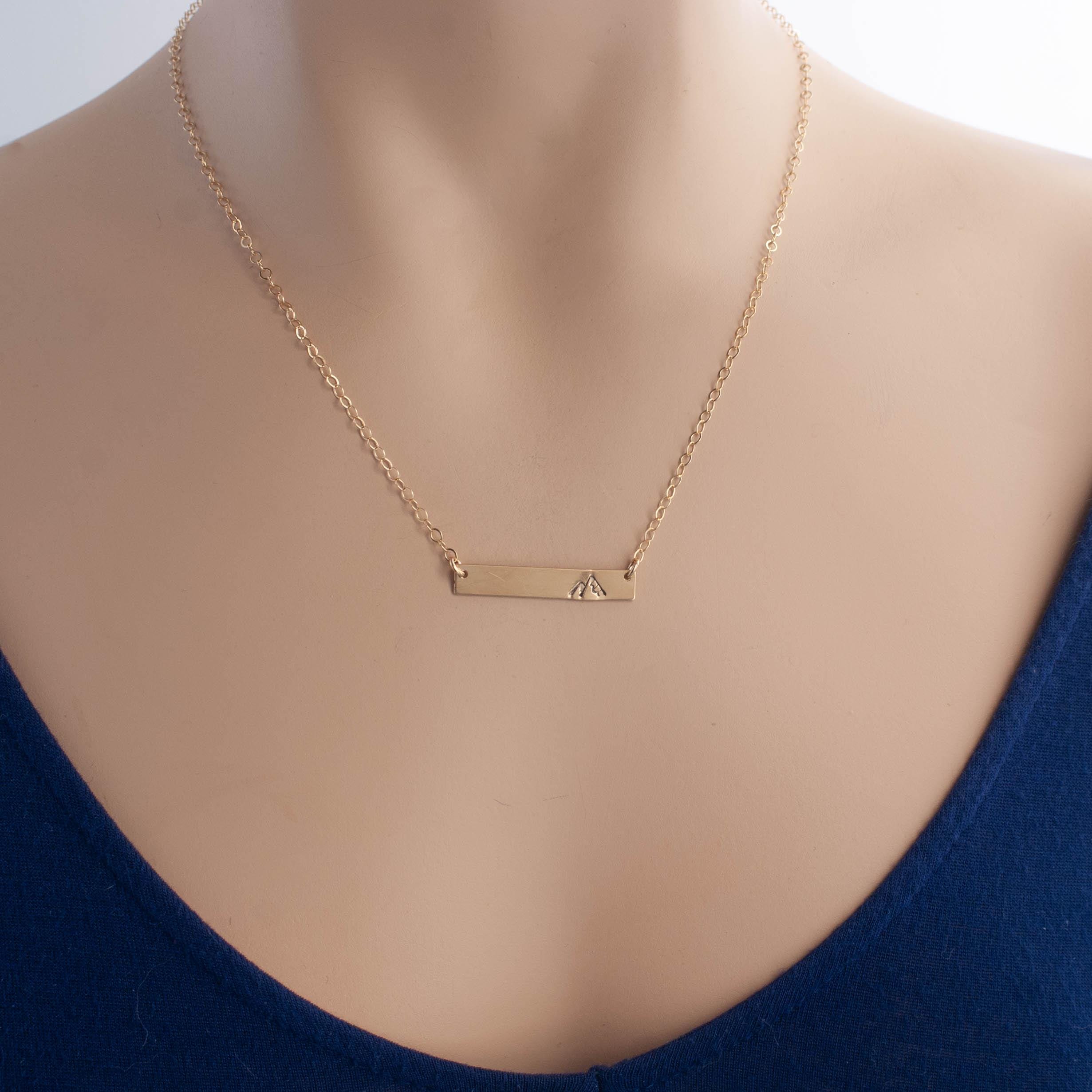Image of gold necklace with mountain stamped on the right side on neck.