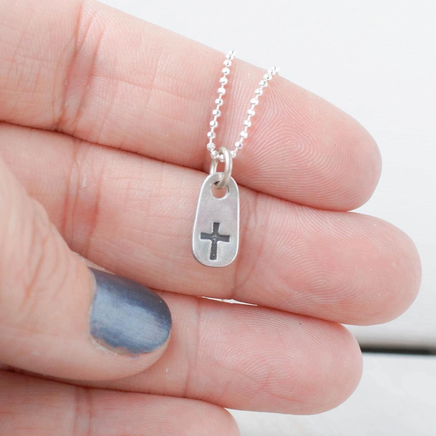 image of tiny cross necklace being held in hand
