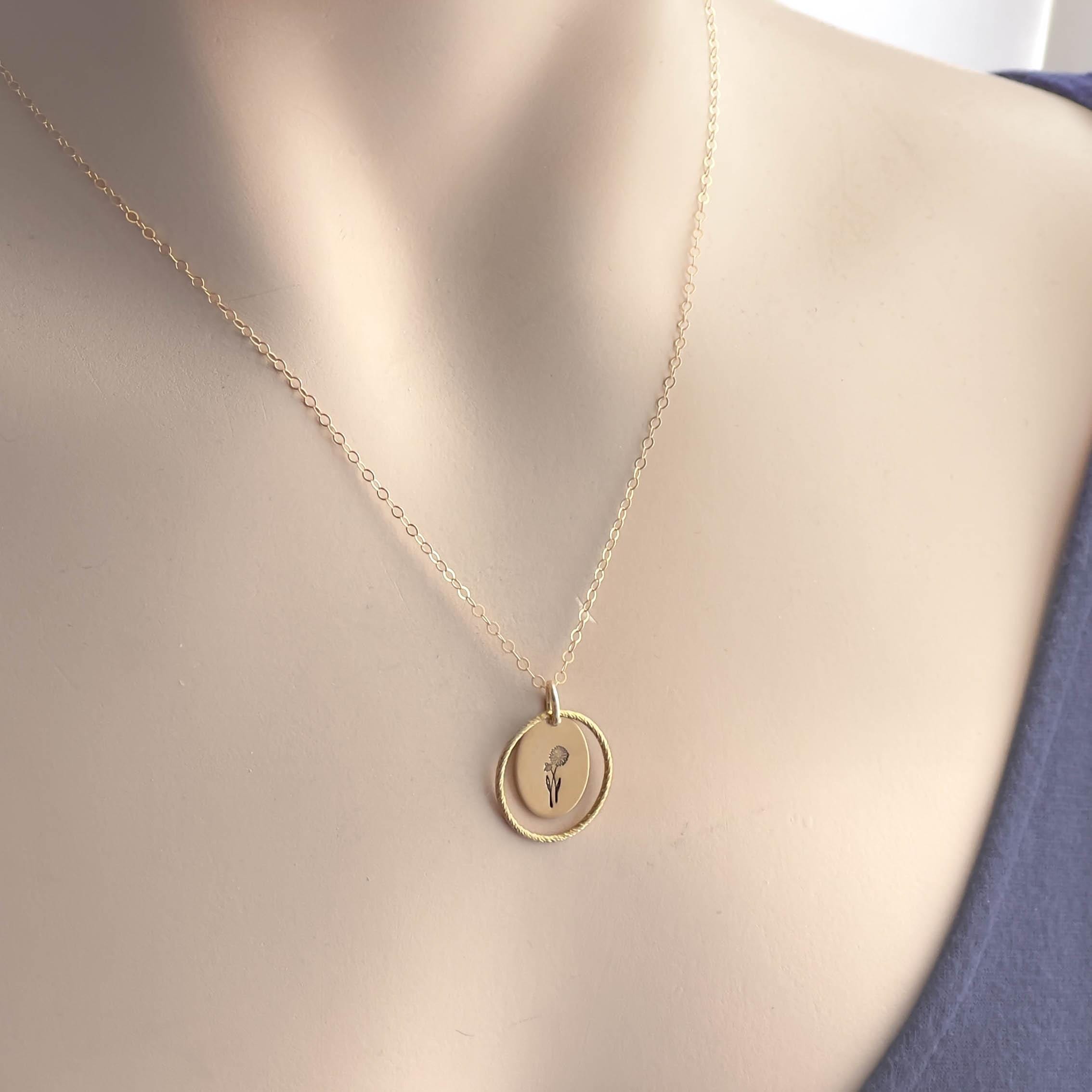 image of an oval gold birth flower necklace with a daisy stamped on it for april and a sparkle oval link surrounding it. the entire necklace is on a mannequin neck