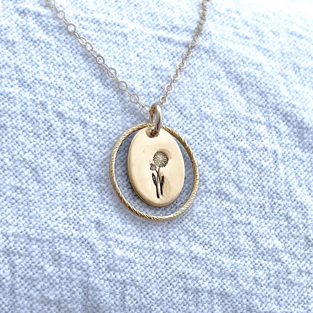 image of an oval gold birth flower necklace with a daisy stamped on it for april and a sparkle oval link surrounding it