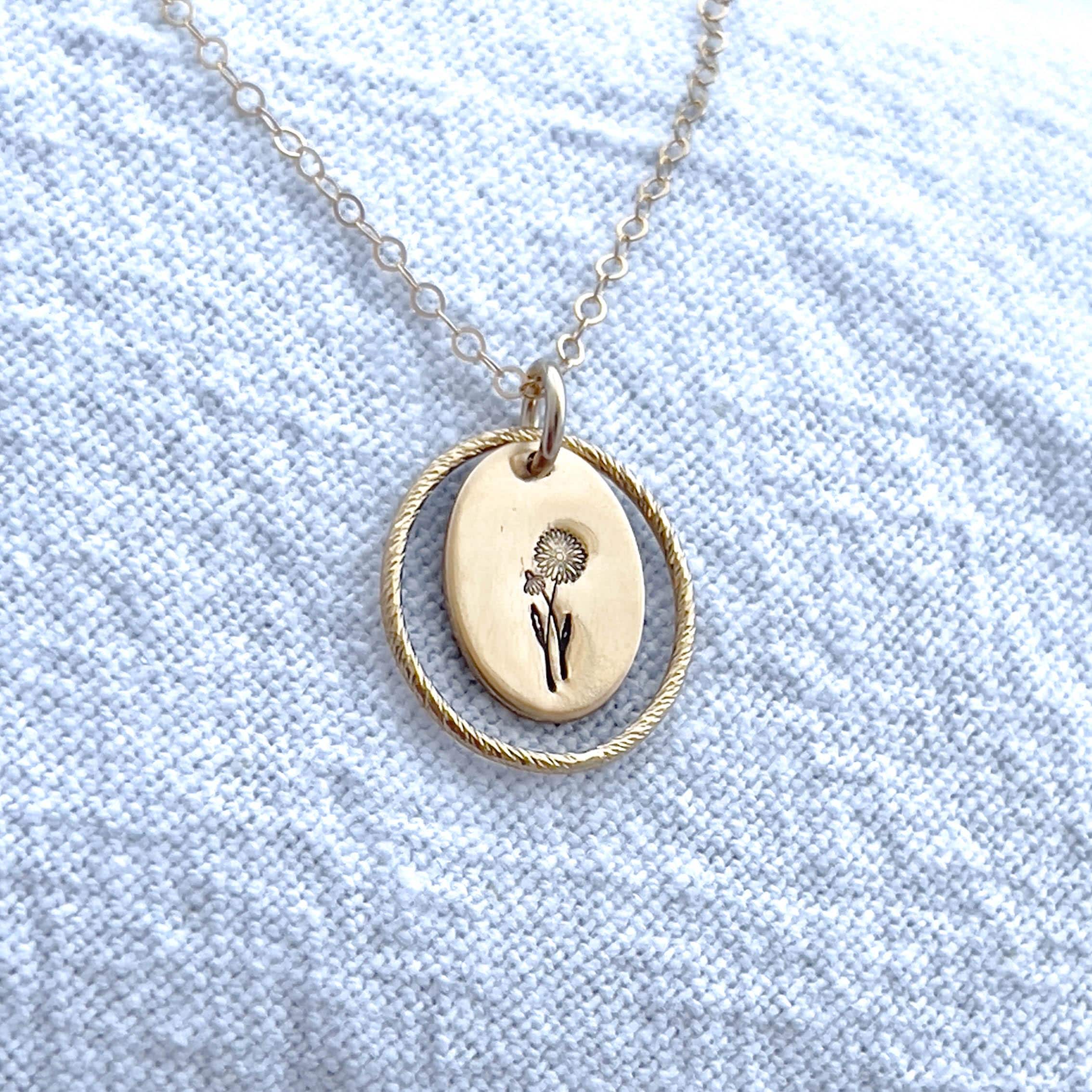 image of an oval gold birth flower necklace with a daisy stamped on it for april and a sparkle oval link surrounding it