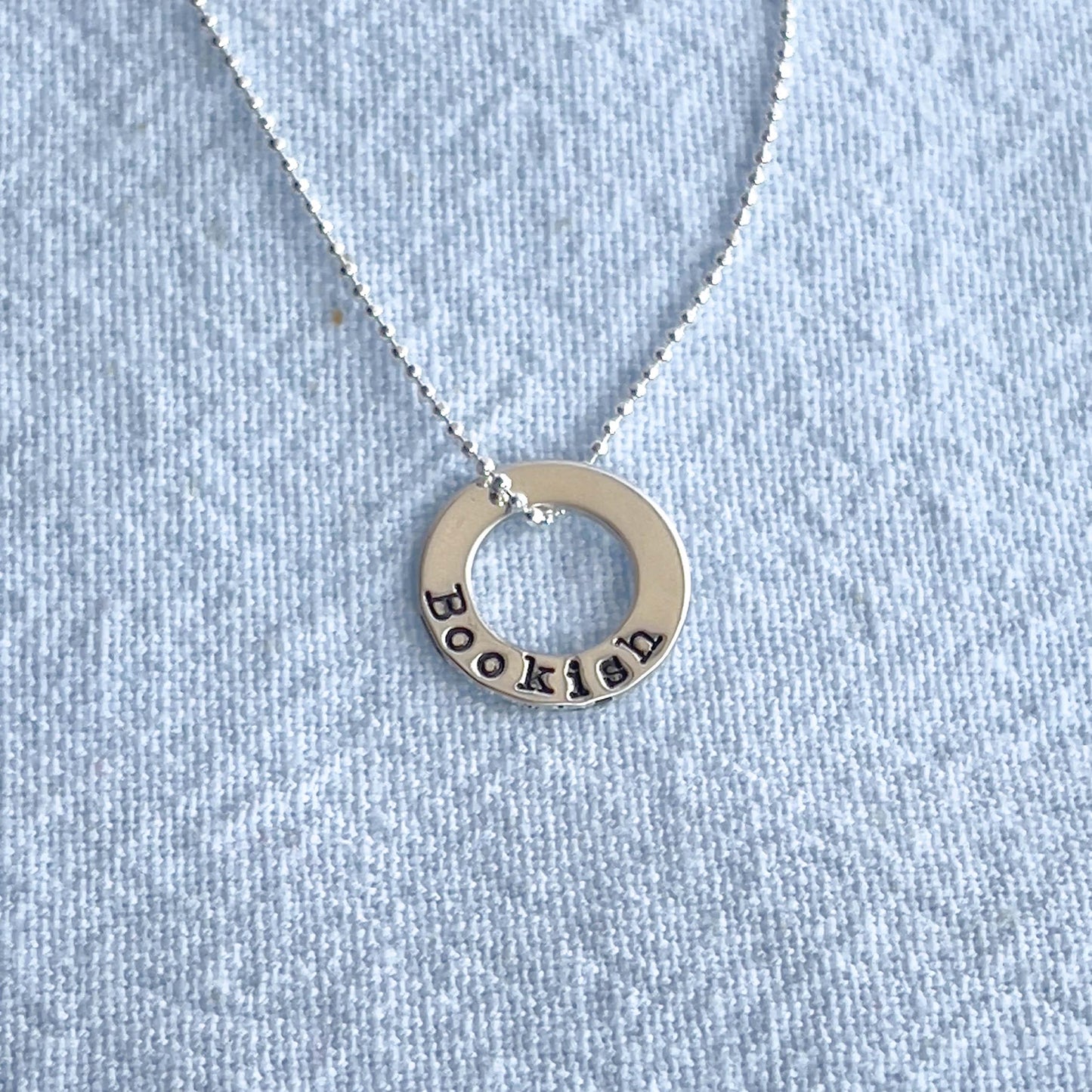 image of bookish sterling silver necklace on blue linen