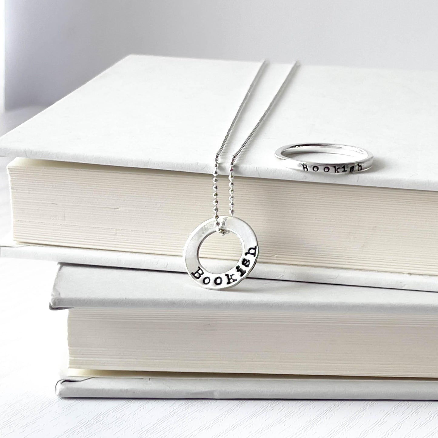 image of bookish sterling silver necklace and bookish ring leaning against books