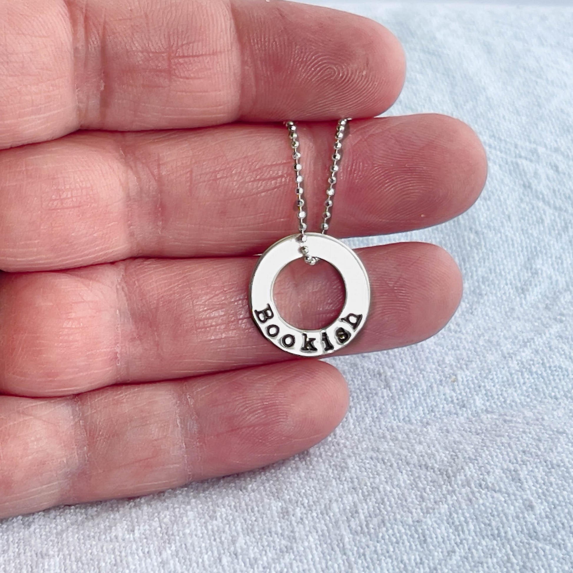 image of bookish sterling silver necklace held in hand