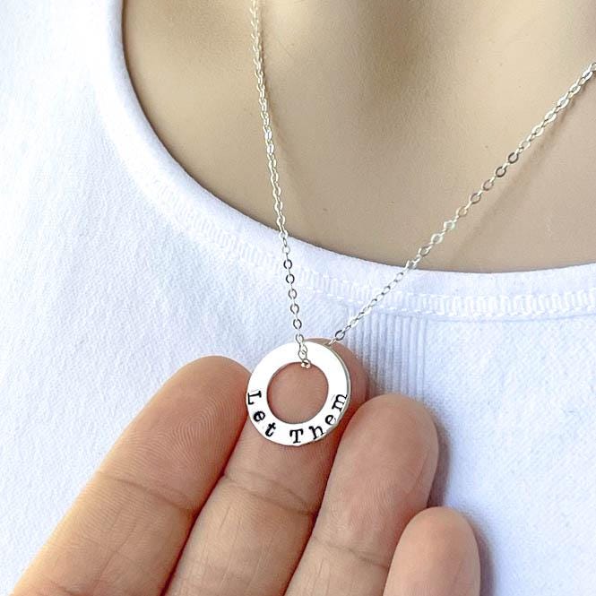 Sterling Silver Necklace stamped with Let Them on hand on white background