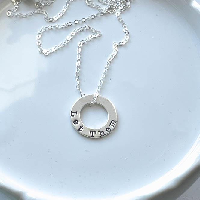 Sterling Silver Necklace stamped with Let Them on white tray