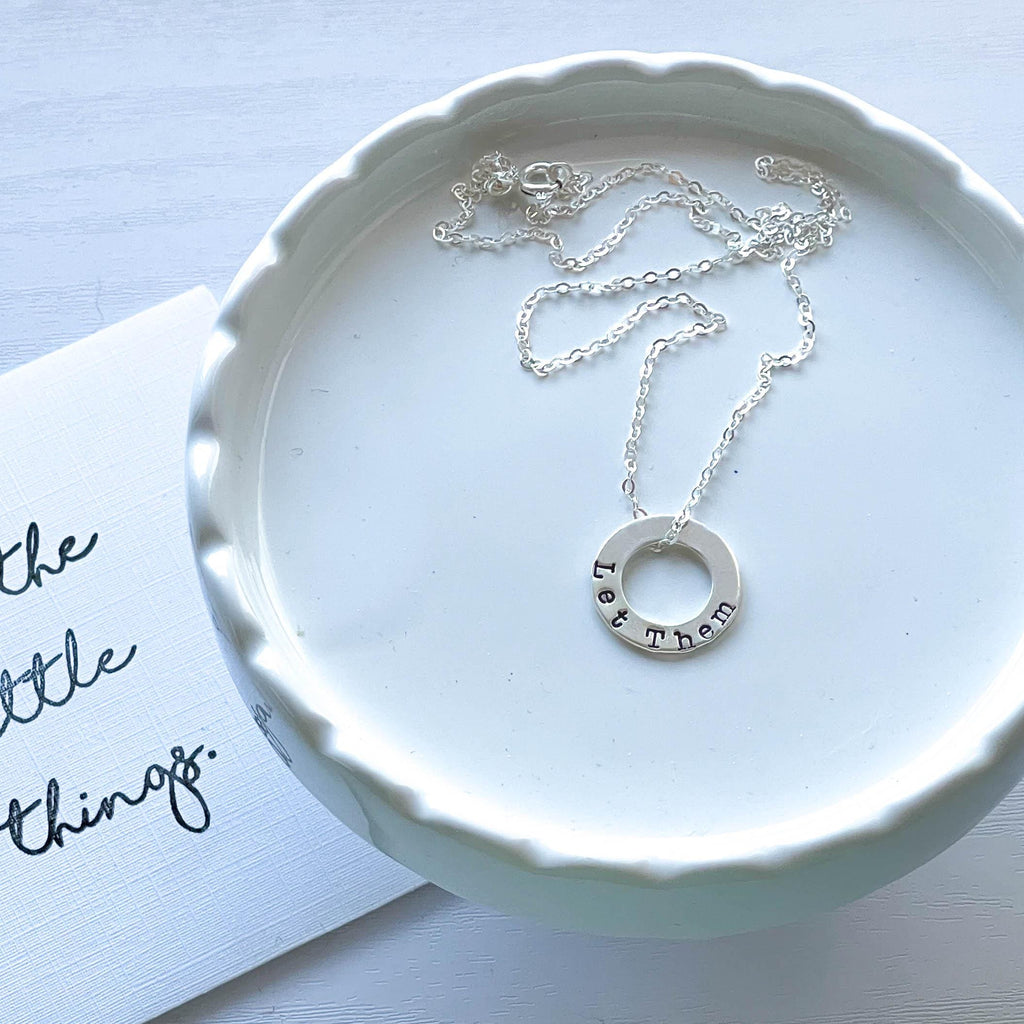 Sterling Silver Necklace stamped with Let Them on white tray with card behind