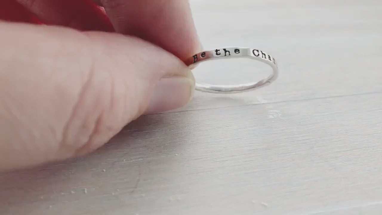 Skinny Stacking Ring handstamped with Be the Change in Sterling Silver on the hand and held in the hand