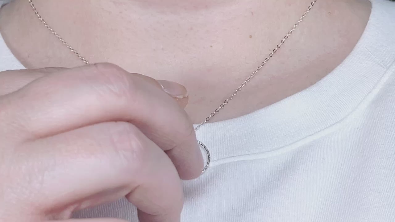 video of hand spinning a silver circle fidget pendant back and forth on a chain