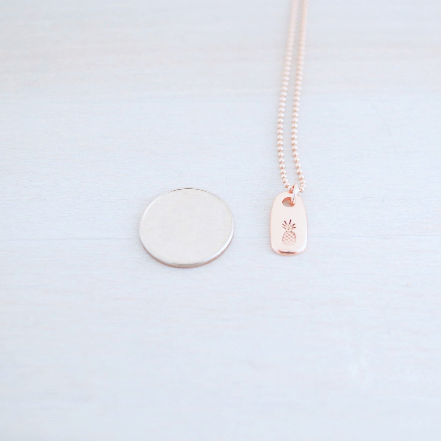 Dainty rose gold pineapple necklace next to dime
