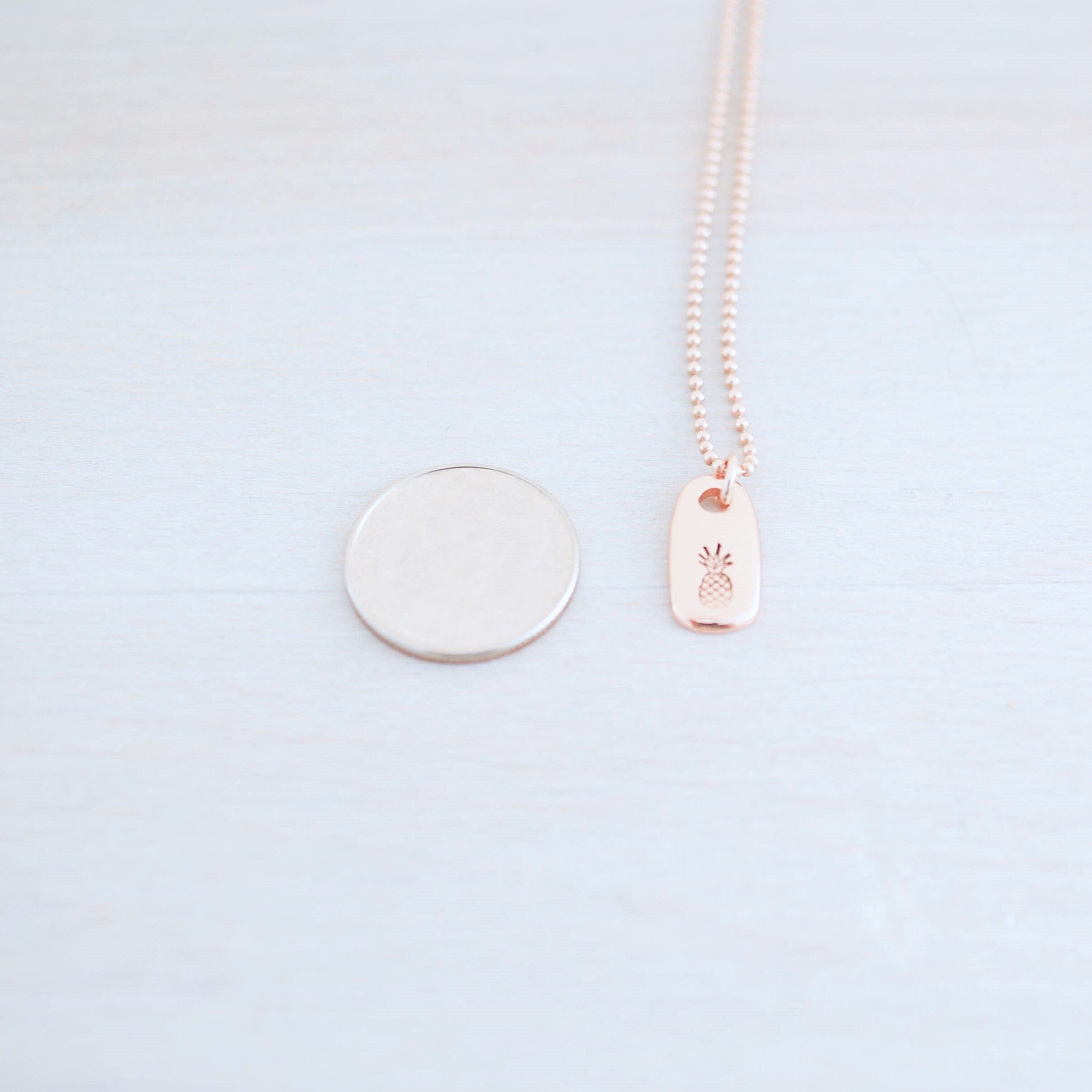 Dainty rose gold pineapple necklace next to dime
