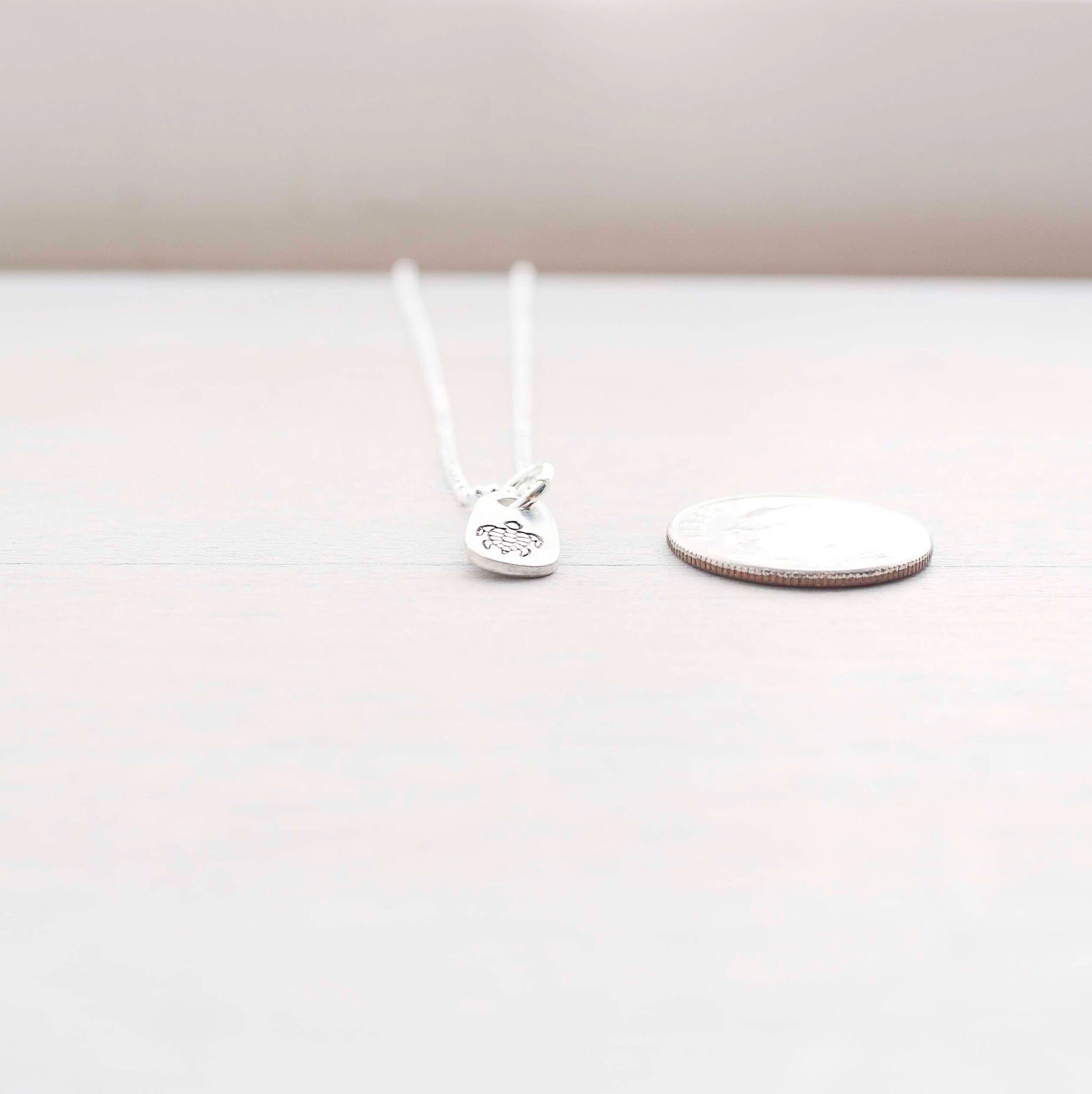 Silver sea turtle necklace in artisan pewter next to a dime