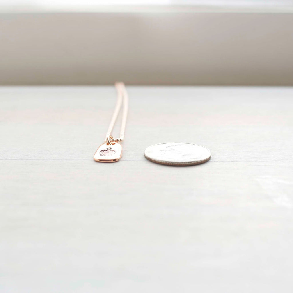 Rose gold necklace stamped with a turtle next to a dime