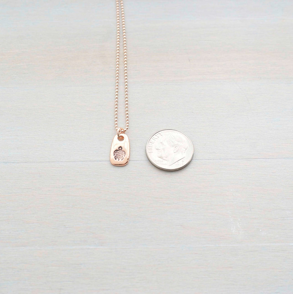 Rose gold necklace stamped with a turtle next to a dime