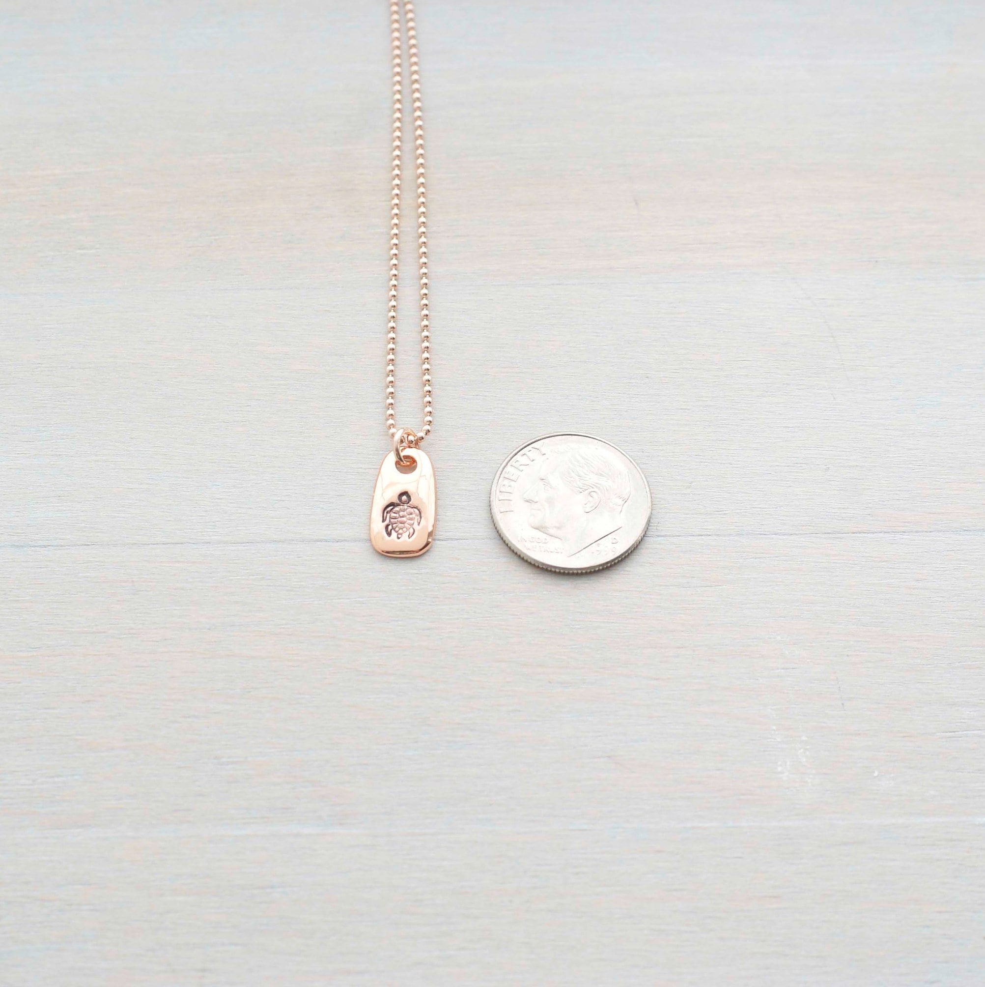 Rose gold necklace stamped with a turtle next to a dime