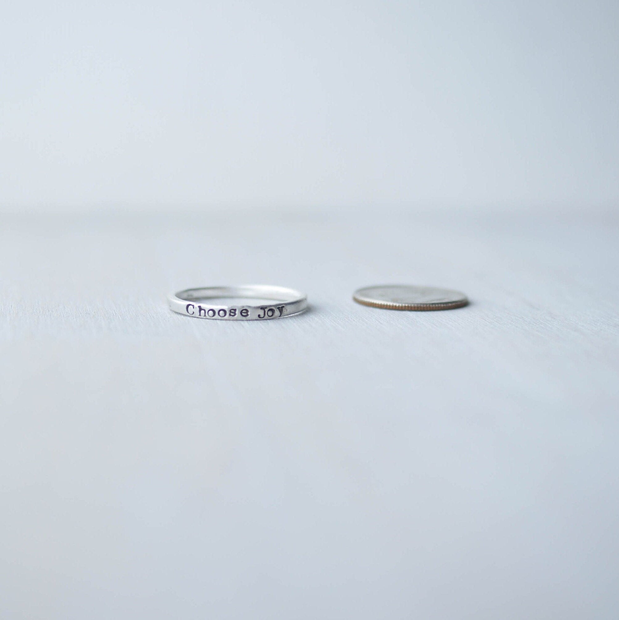 Stacking ring in Sterling silver handstamped with Choose Joy next to dime