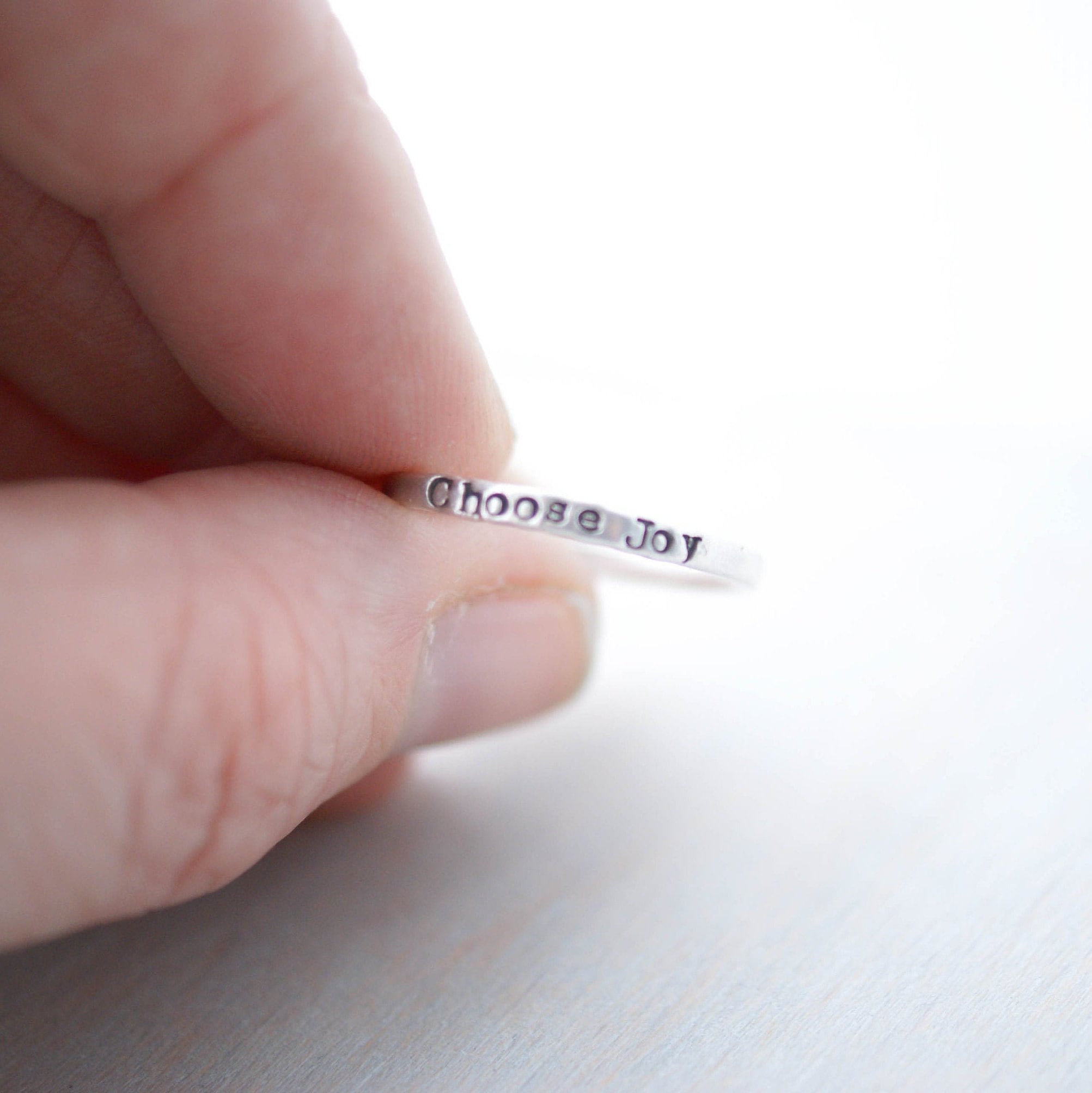 Stacking ring in sterling silver stamped with choose joy held in between fingers