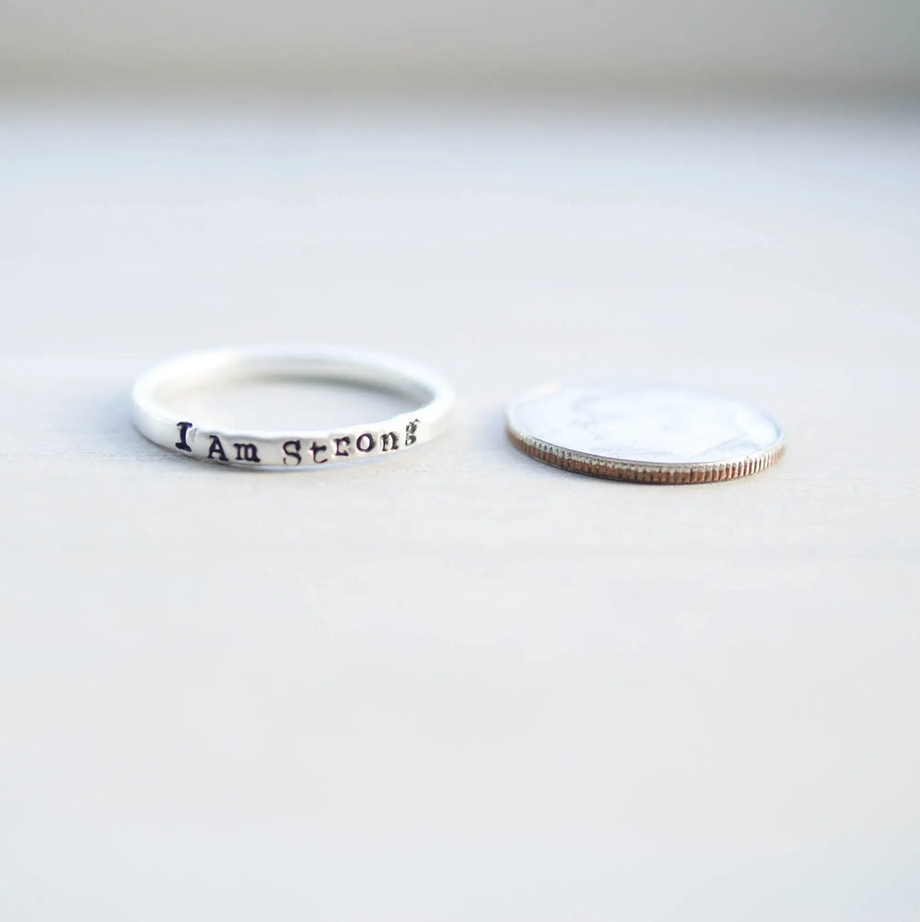 Sterling Silver stacking ring handstmaped with I Am Strong next to dime