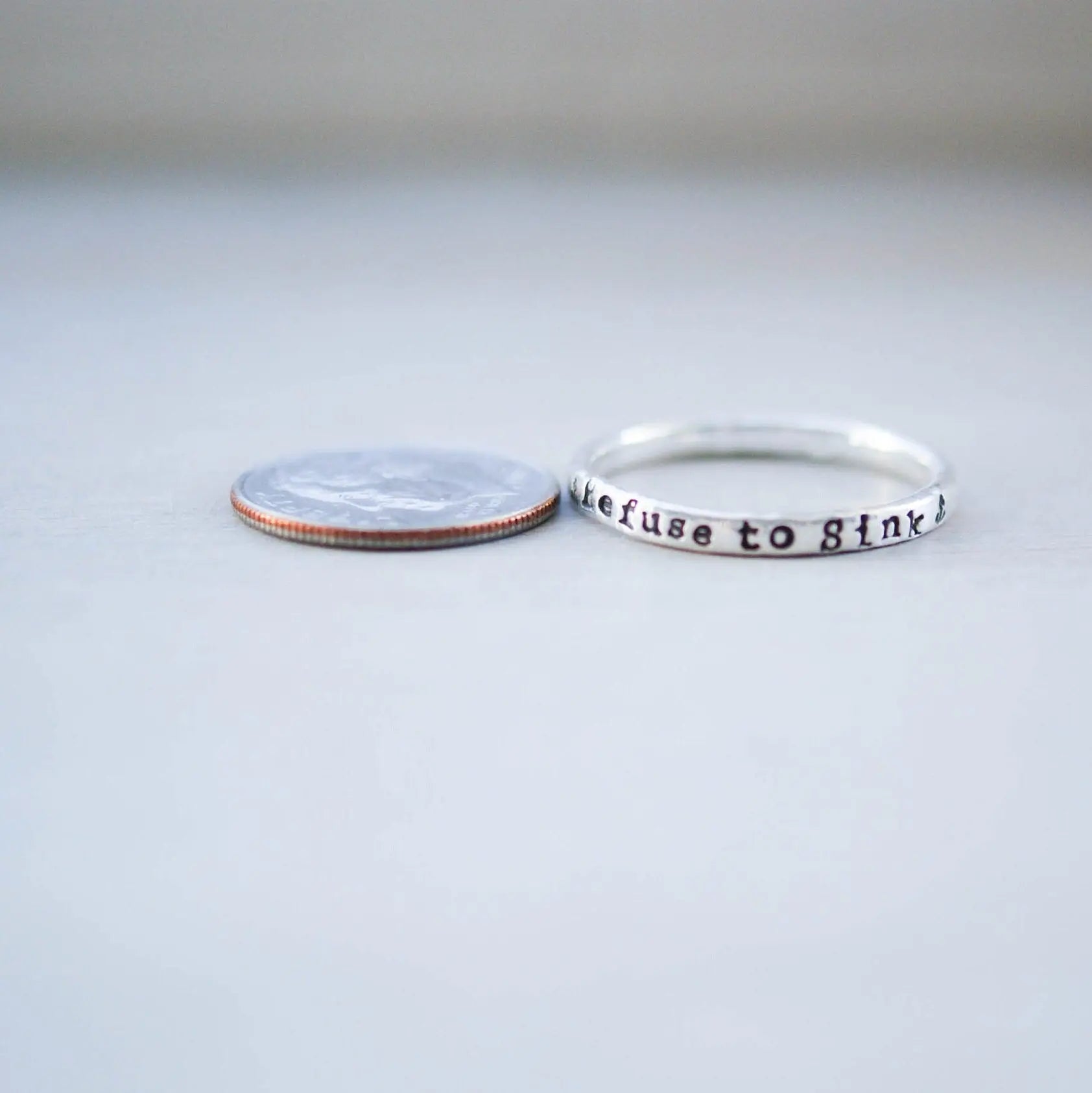 Sterling silver ring handstamped with Refuse to sink next to dime