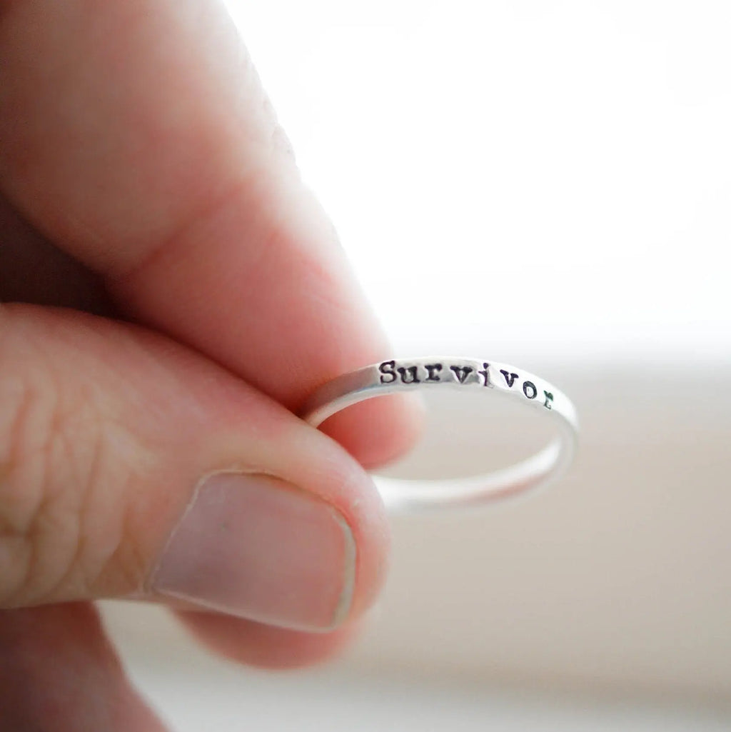 Sterling silver ring stamped with Survivor held between fingers