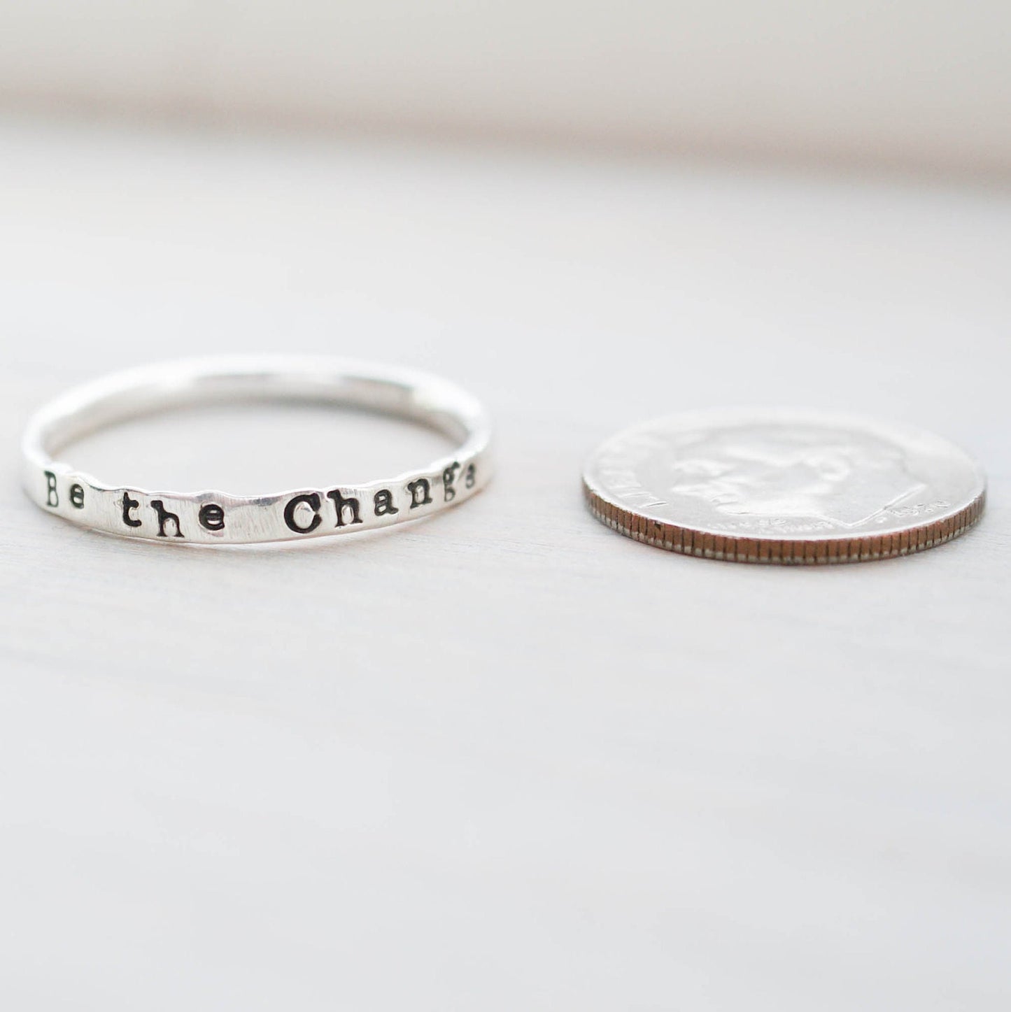 Skinny Stacking Ring handstamped with Be the Change in Sterling Silver next to dime for scale