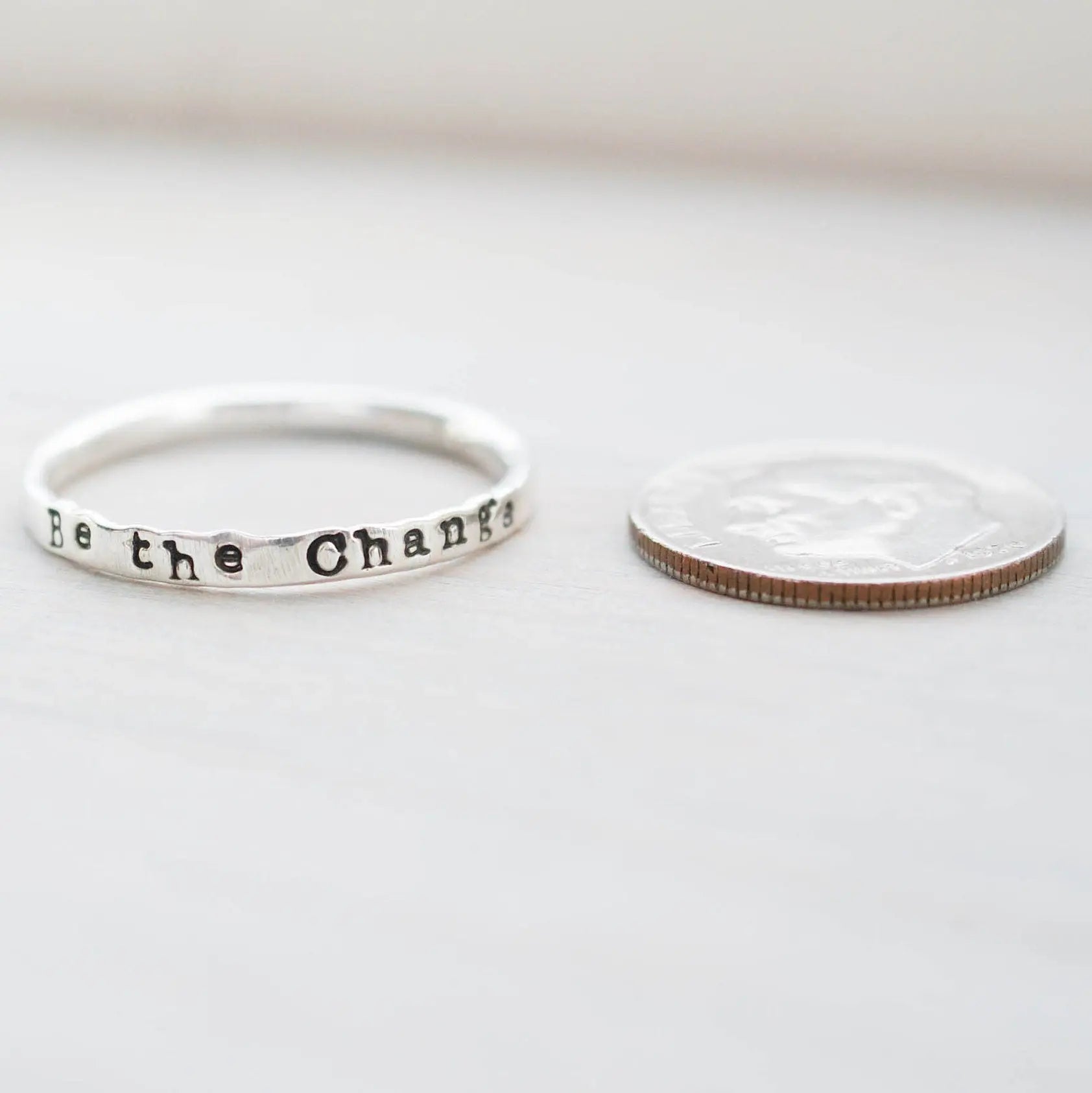 Skinny Stacking Ring handstamped with Be the Change in Sterling Silver next to dime for scale