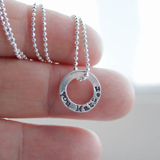 Tiny circle necklace in sterling silver stamped with You Matter held in hand