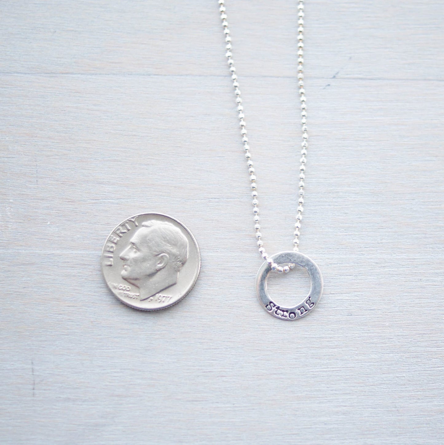 Sterling silver tiny circle stamped with Strong necklace next to dime