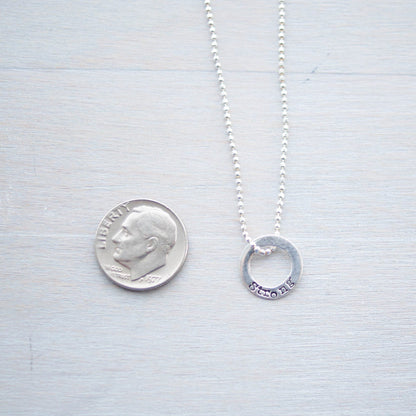 Sterling silver tiny circle stamped with Strong necklace next to dime