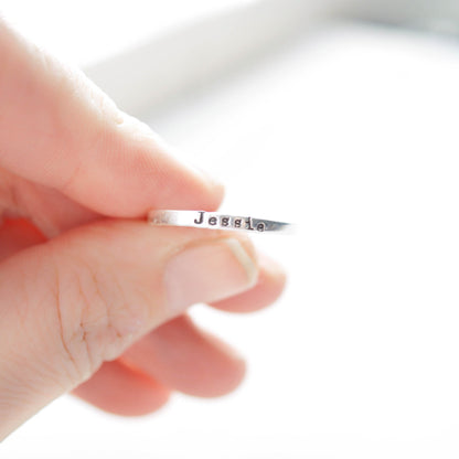 Sterling silver ring stamped with a personalized name held between fingers